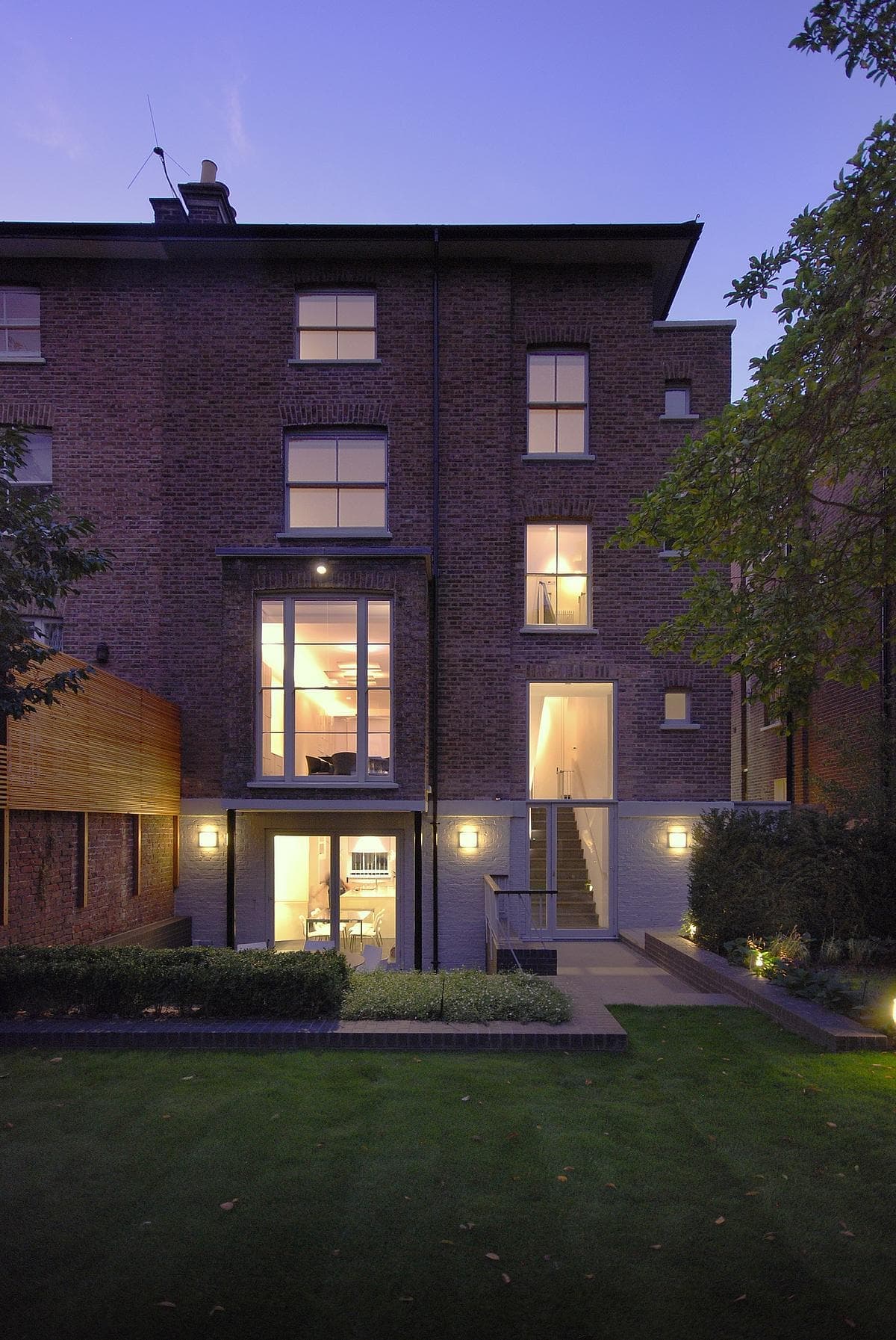 Rear brick elevation at dusk with illuminated windows and glazed doors facing the garden.