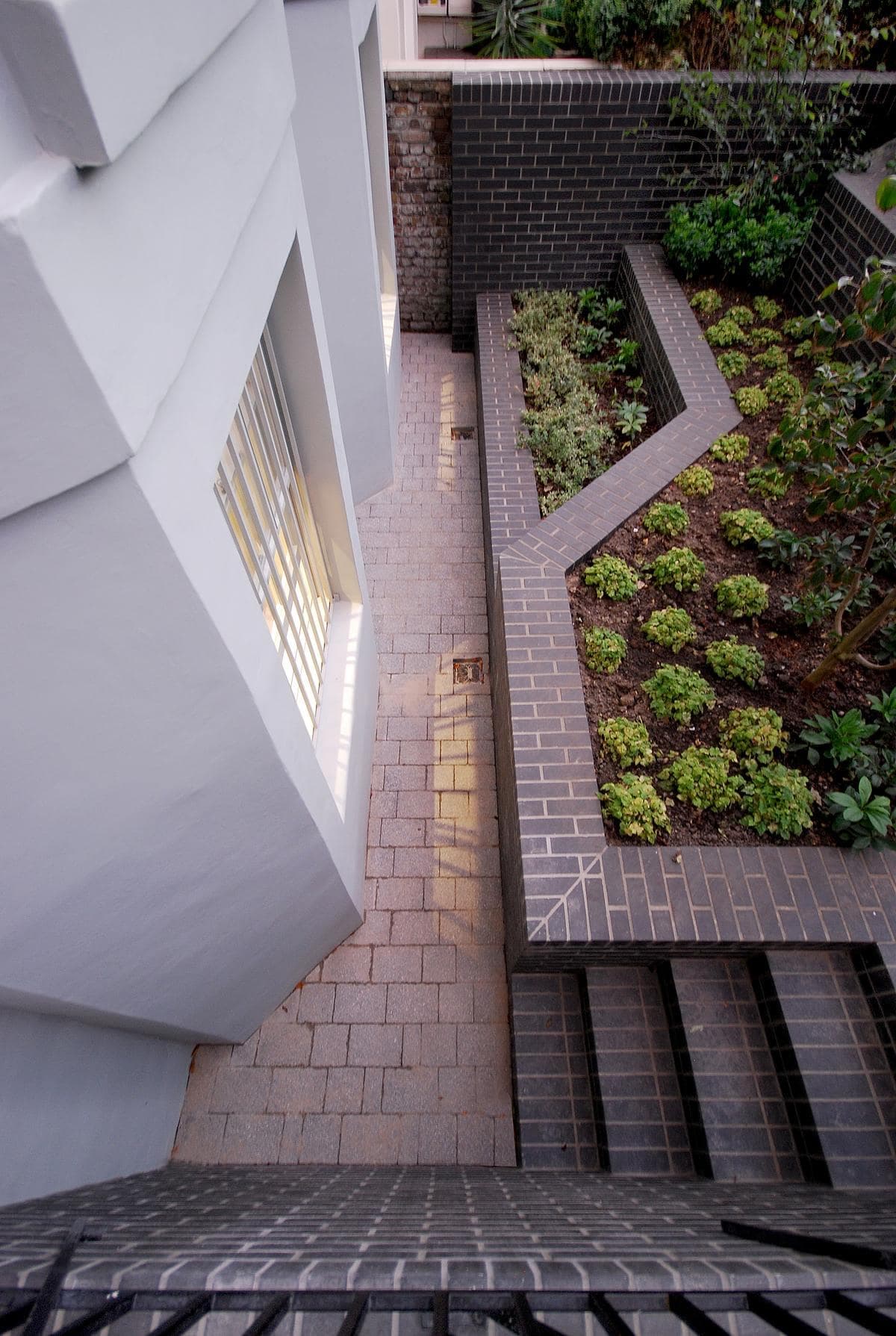 View down into a paved lower courtyard beside brick steps and raised planting beds.