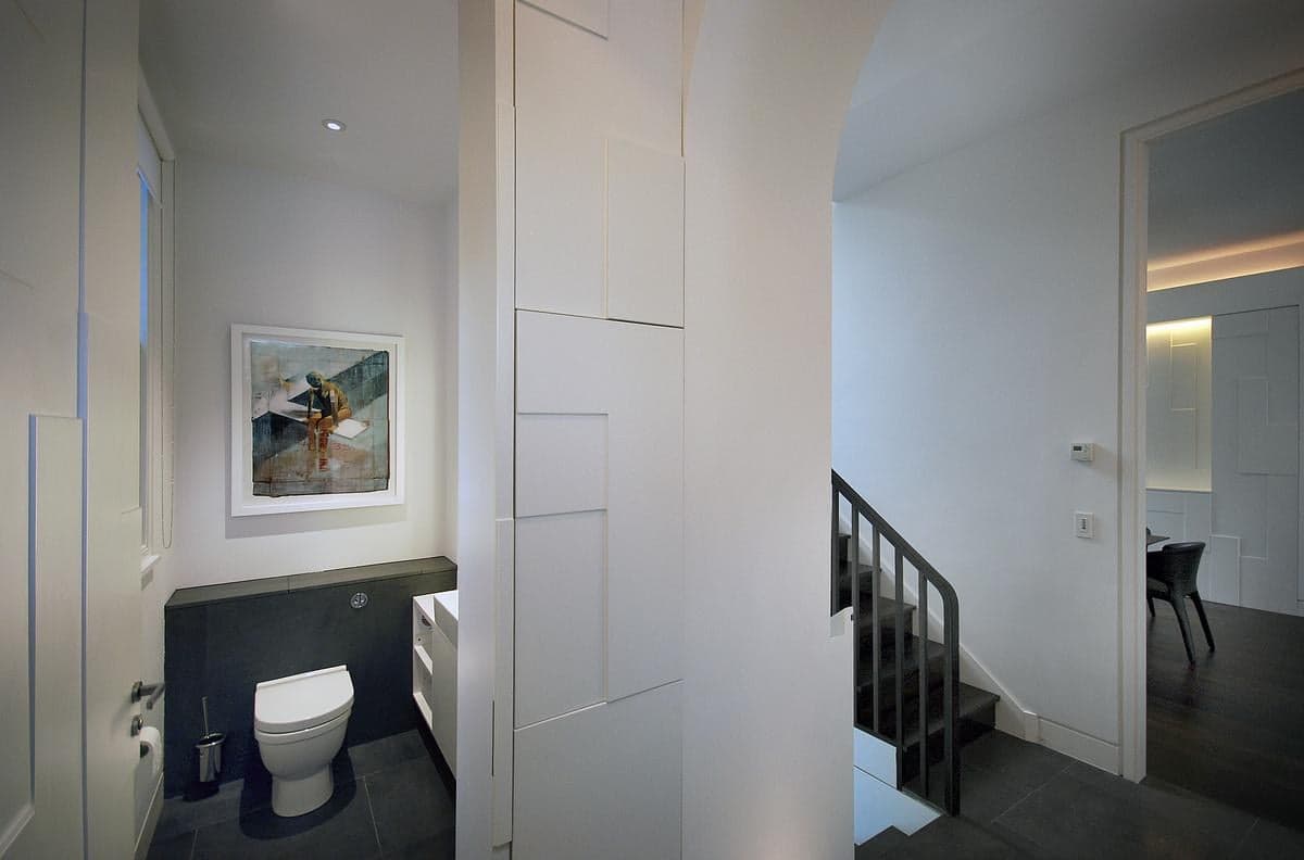 White hallway with a concealed panelled door, staircase and adjoining cloakroom.