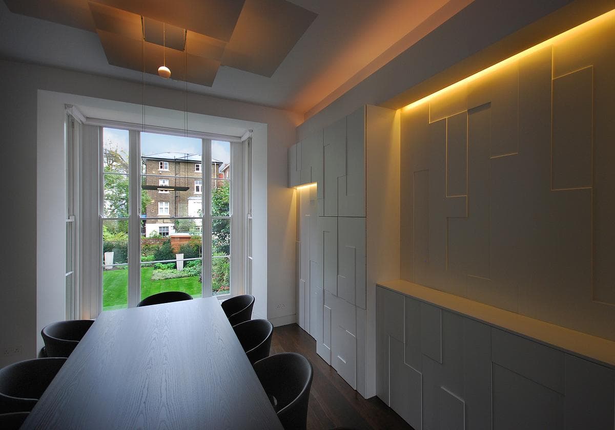Dark dining table beneath pendant lights, with illuminated wall panelling and doors to the garden.